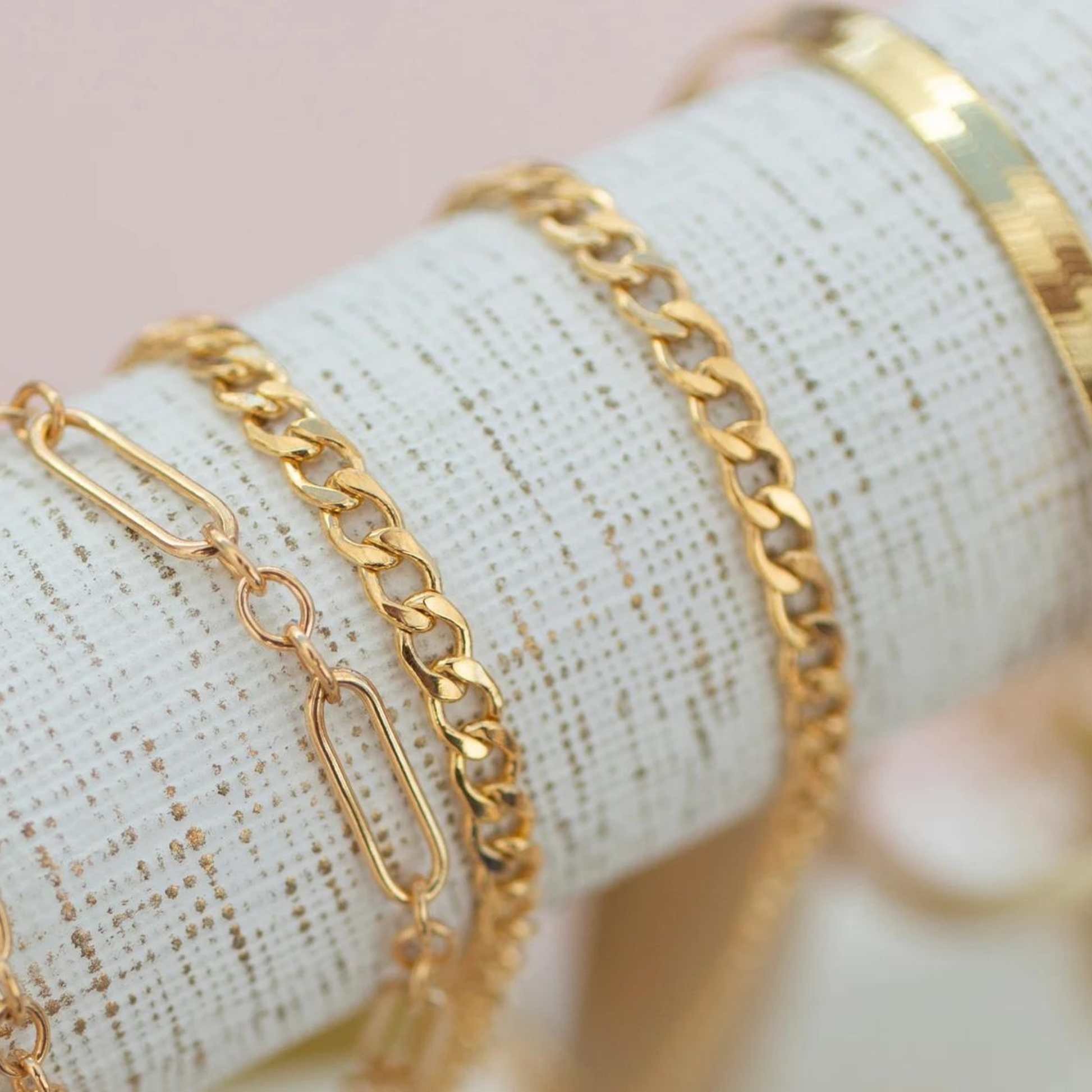 Gold chain bracelets on a textured surface with a pink background